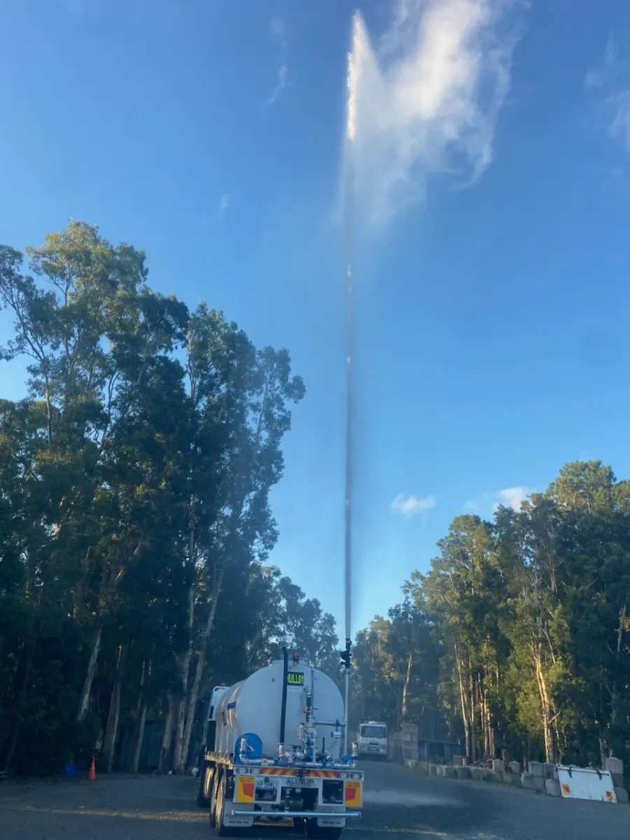 A Simon Hull water truck firing a tall vertical spray of water high into a clear blue sky